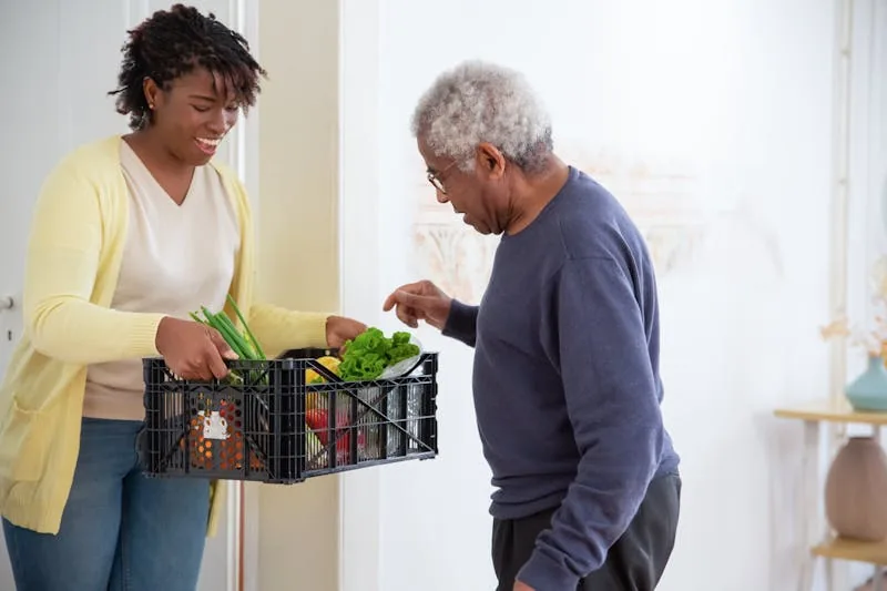 Carer bringing groceries to an elderly gentleman at his home