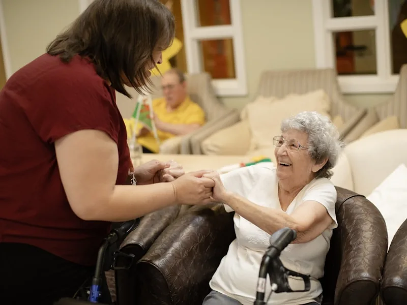 Carer holding hands with a smiling elderly woman providing compassionate support