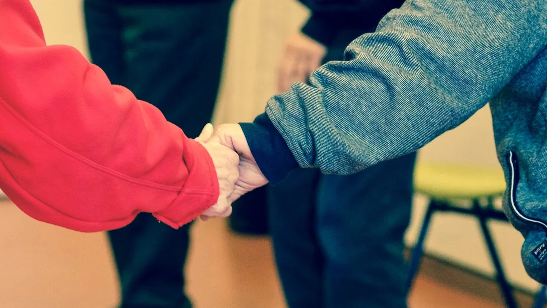 A care worker gently holds an older person's hands during a home visit