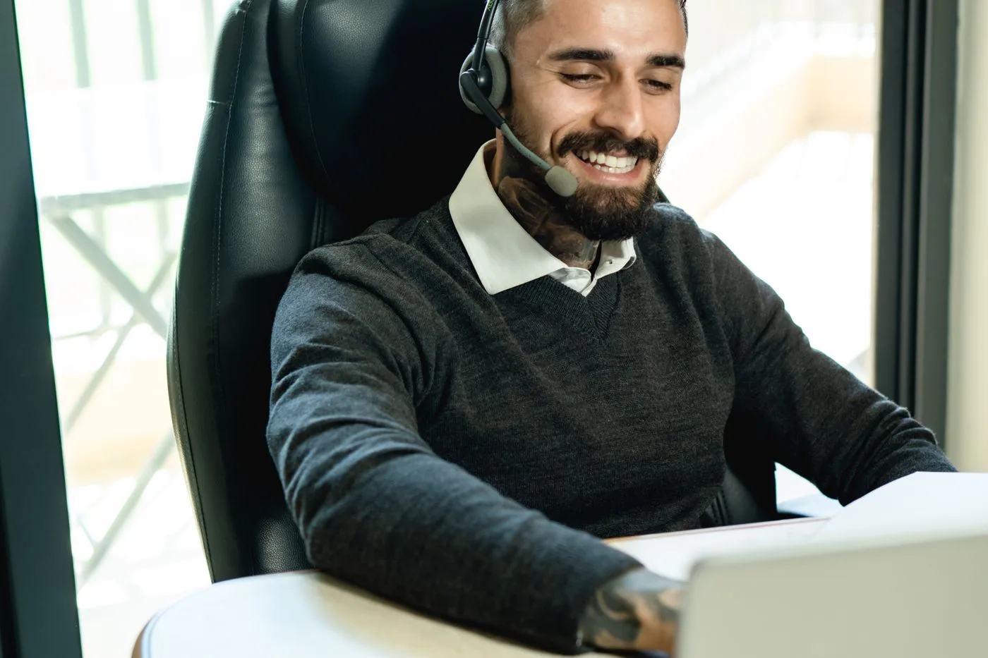 A care coordinator wearing a headset, smiling while working at a laptop in an office